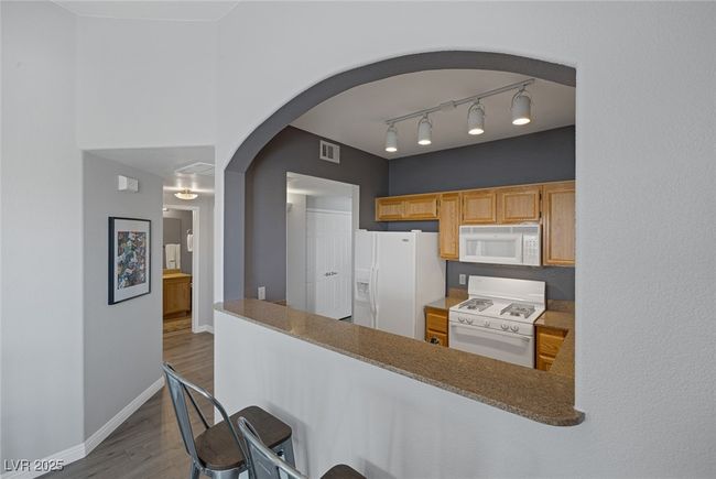 Kitchen featuring white appliances, arched walkways, dark wood finished floors, baseboards, and visible vents | Image 10