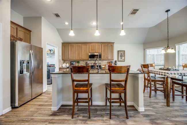 Kitchen featuring a center island with sink, light wood-type flooring, dark stone countertops, stainless steel appliances, and decorative backsplash | Image 4