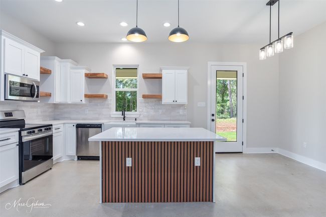 Kitchen featuring open shelves, backsplash, finished concrete flooring, and appliances with stainless steel finishes | Image 4