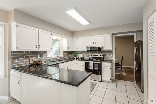 Kitchen featuring a sink, backsplash, stainless steel appliances, white cabinets, and a peninsula | Image 7