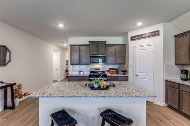 Kitchen View 1 featuring stainless steel appliances, light laminated wood plank floors, backsplash, and a center island with 2 sided stainless steel sink | Image 7