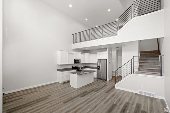 Kitchen with stainless steel appliances, open floor plan, dark countertops, a towering ceiling, and light wood-type flooring | Image 7
