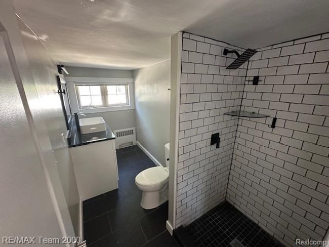Full bathroom featuring radiator heating unit, a stall shower, and dark tile patterned flooring | Image 23