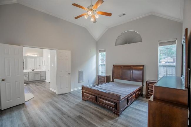 This spacious master bedroom suite features a high vaulted ceiling, neutral walls, and laminate flooring . It includes a ceiling fan and large windows for natural light. The room leads into an ensuite bathroom, creating a comfortable and functional space. | Image 27