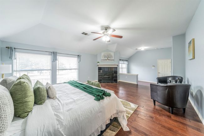 Bedroom with vaulted ceiling, multiple windows, wood-type flooring, a fireplace, and ceiling fan | Image 22