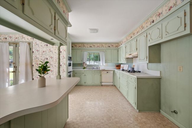 Kitchen with green cabinetry, white appliances, under cabinet range hood, light floors, and wallpapered walls | Image 15