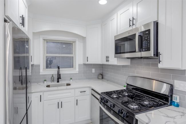 Kitchen with light stone countertops, white cabinets, appliances with stainless steel finishes, and sink | Image 18