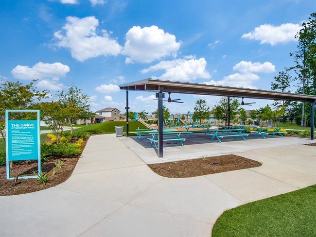 Community park area featuring a covered pavilion with picnic tables, ceiling fans, and a nearby playground. The setting is surrounded by landscaped greenery, with a clear path leading through the space. Ideal for outdoor gatherings and picnics and birthdays | Image 16