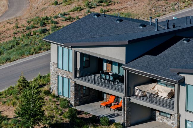 Back of property with stone siding, a balcony, roof with shingles, stucco siding, and a patio area | Image 5