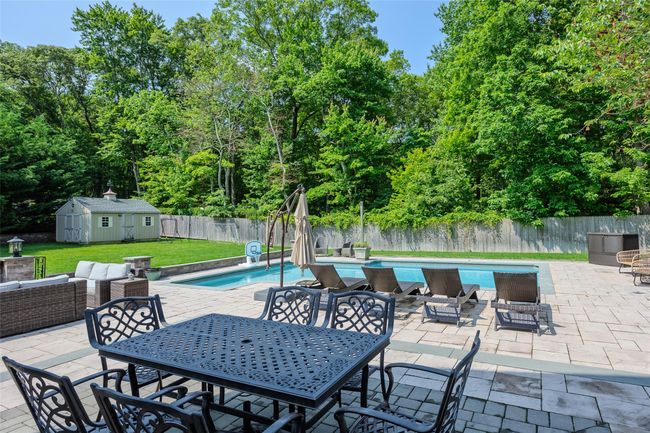 Fenced backyard with a patio, outdoor dining space, an outdoor living space, a shed, and view of scattered trees | Image 44