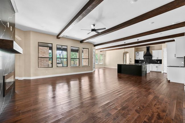 Unfurnished living room with ceiling fan, a premium fireplace, dark wood-style flooring, baseboards, and beamed ceiling | Image 20