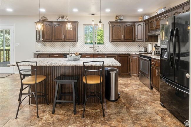 Kitchen featuring electric range, black fridge with ice dispenser, a kitchen island, tasteful backsplash, and tile patterned floors | Image 8