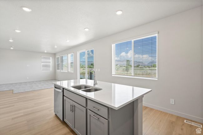 Kitchen featuring gray cabinets, stainless steel dishwasher, light wood-style flooring, light countertops, and a kitchen island with sink | Image 18