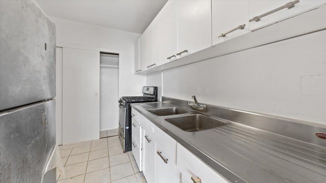 Kitchen featuring white cabinets, appliances with stainless steel finishes, light tile patterned flooring, a sink, and dark countertops | Image 11