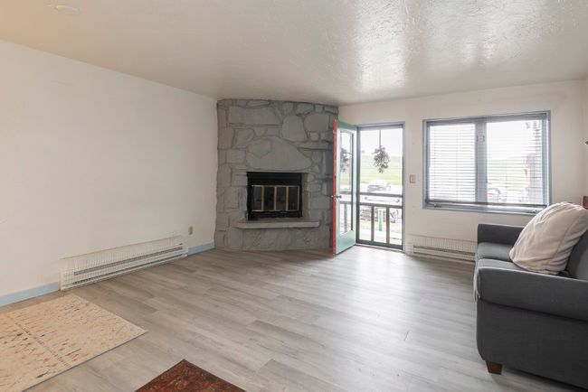 Living area with baseboard heating, wood finished floors, a stone fireplace, and a textured ceiling | Image 13
