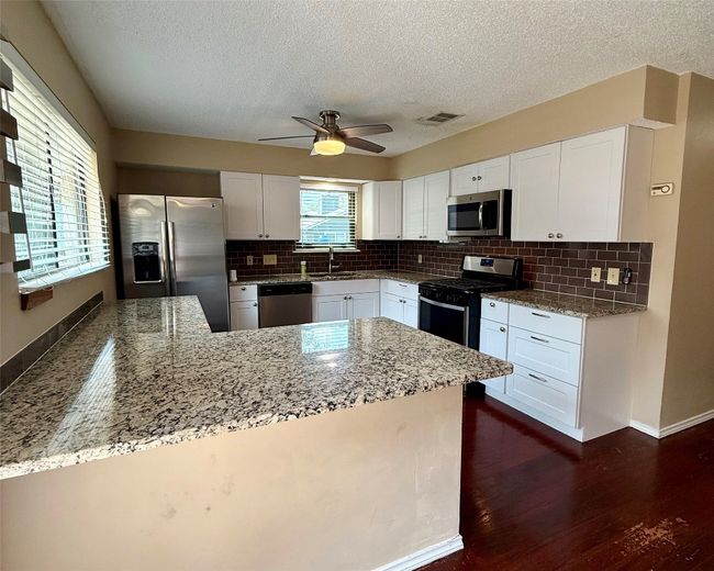 Kitchen with stainless steel appliances, a sink, a peninsula, a textured ceiling, and tasteful backsplash | Image 7