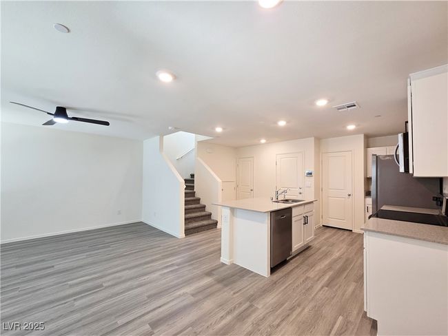 Kitchen featuring stainless steel appliances, a sink, an island with sink, light wood finished floors, and white cabinets | Image 7