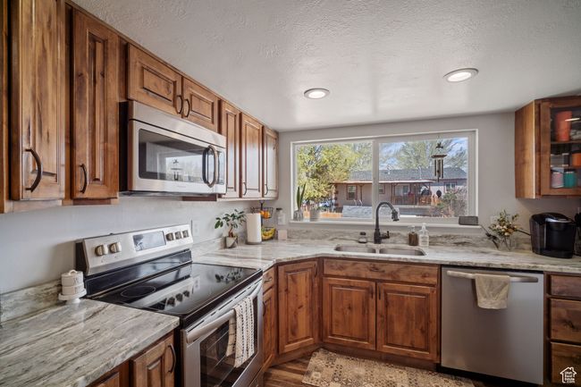 Kitchen with light stone counters, stainless steel appliances, brown cabinets, a sink, and a textured ceiling | Image 6