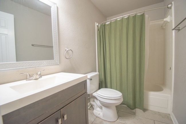 Full bath featuring vanity, shower / bath combo, toilet, a textured wall, and tile patterned flooring | Image 12