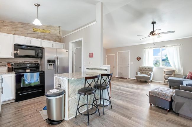 Kitchen with black appliances, open floor plan, white cabinets, light wood finished floors | Image 12