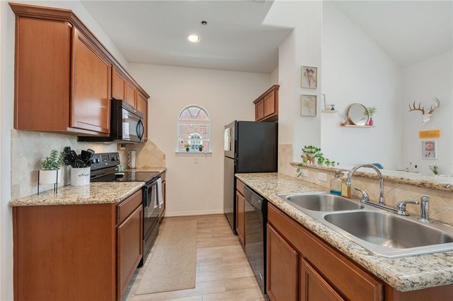 Kitchen featuring black appliances, light wood finished floors, backsplash, brown cabinets, and lofted ceiling | Image 8