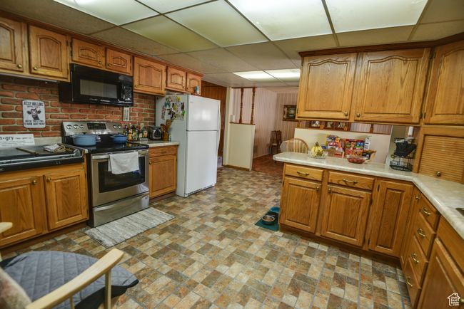 Kitchen featuring stainless steel electric range oven, black microwave, freestanding refrigerator, brown cabinets, and light countertops | Image 27