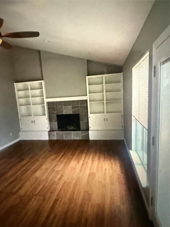 Unfurnished living room featuring lofted ceiling, a ceiling fan, wood finished floors, and a fireplace | Image 8