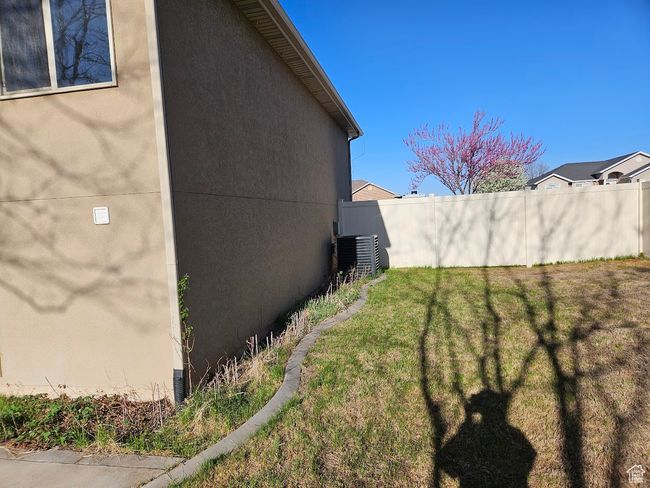 View of side of property with stucco siding, central air condition unit, a lawn, and fence | Image 80