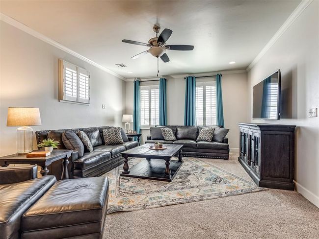 Carpeted living area with visible vents, crown molding, baseboards, and ceiling fan | Image 24