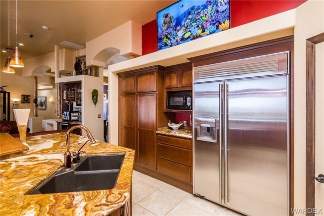 Kitchen with stainless steel built in refrigerator, black microwave, light tile patterned floors, decorative light fixtures, and light stone countertops | Image 37