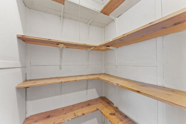 This photo shows a small, well-organized pantry with wooden shelves on three walls, providing ample storage space for kitchen essentials. | Image 17