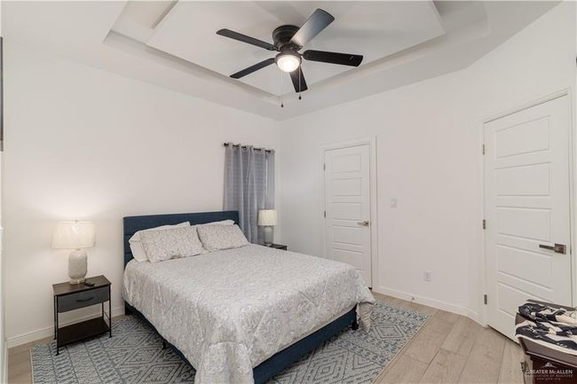Bedroom with light wood-style floors, a ceiling fan, and a raised ceiling | Image 7