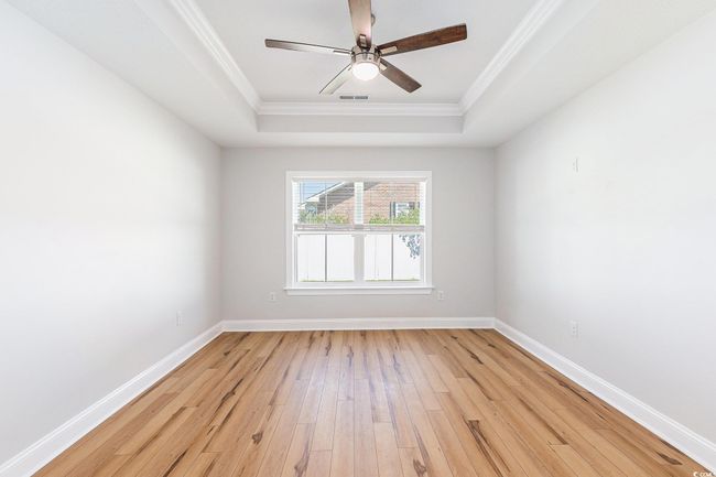 Spare room featuring a raised ceiling, ornamental molding, light wood-style floors, and a ceiling fan | Image 15