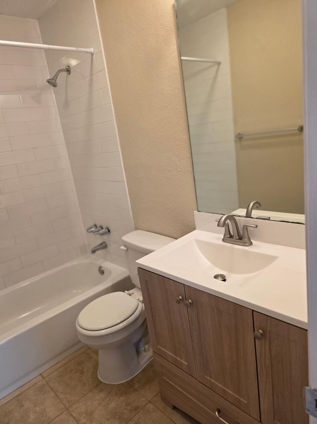 Full bathroom featuring vanity, shower / tub combination, a textured wall, and tile patterned flooring | Image 15