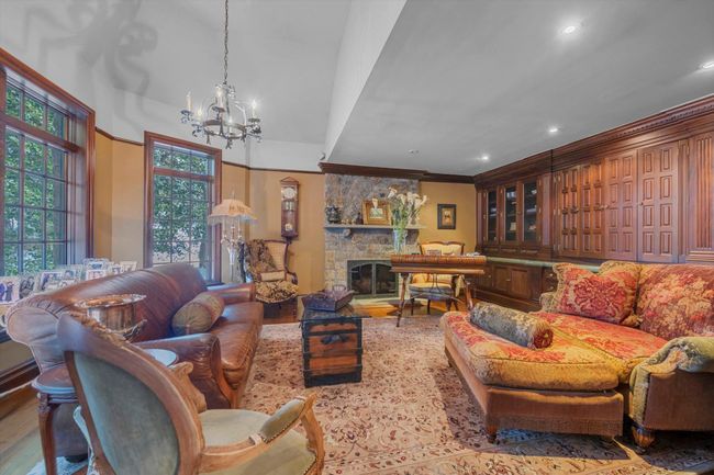 Living room with crown molding, a notable chandelier, a stone fireplace, and light wood-type flooring | Image 12