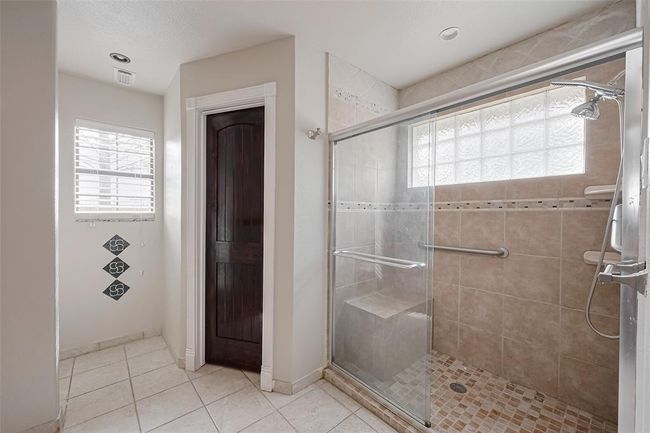 Enjoy the spacious walk-in shower with built-in bench, glass enclosure, and tile surround. A glass block window provides natural light while maintaining privacy. | Image 28
