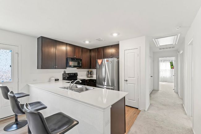 Kitchen featuring black appliances, dark brown cabinets, light countertops, a peninsula, and light wood-style floors | Image 13