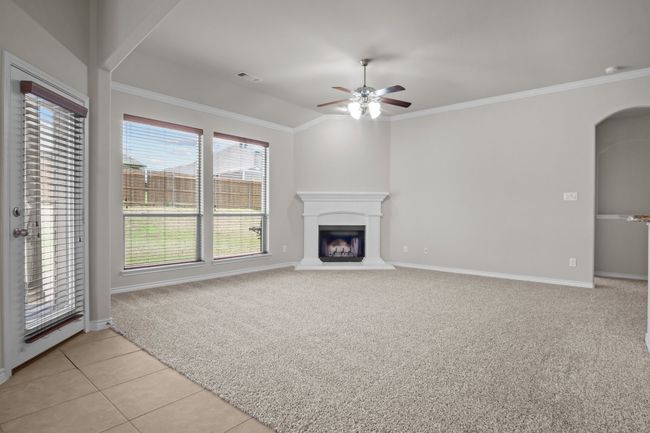 Unfurnished living room with crown molding, visible vents, baseboards, ceiling fan, and a fireplace with raised hearth | Image 18