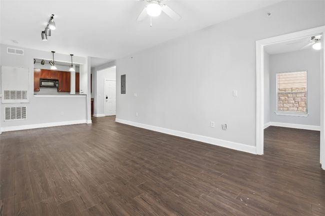 Unfurnished living room with dark wood-type flooring, electric panel, a ceiling fan, and visible vents | Image 12