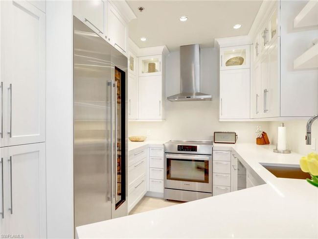 Kitchen with wall chimney range hood, range, high quality fridge, a sink, and white cabinets | Image 15