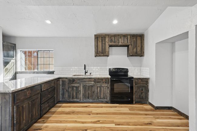 Kitchen with light stone counters, light wood finished floors, electric range, a sink, and dark brown cabinetry | Image 8