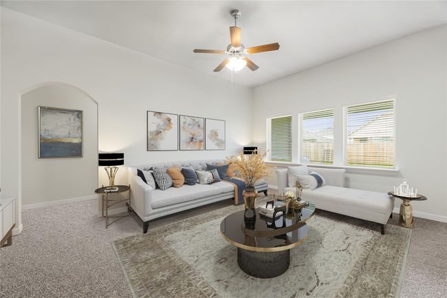 This open living room offers a welcoming feel with tall ceilings, a ceiling fan with lights, neutral tones, and oversized windows that brighten up the entire space. *Virtually Staged | Image 4