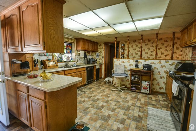 Kitchen with electric stove, wallpapered walls, dishwasher, a drop ceiling, and light countertops | Image 29