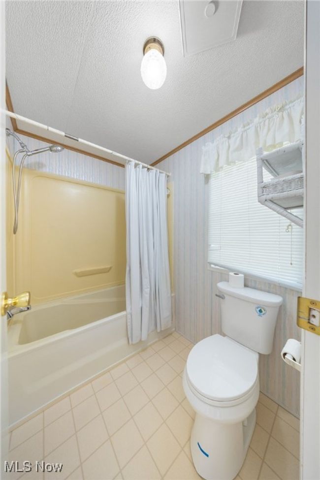 Bathroom with toilet, tile patterned flooring, shower / bath combo with shower curtain, and a textured ceiling | Image 11
