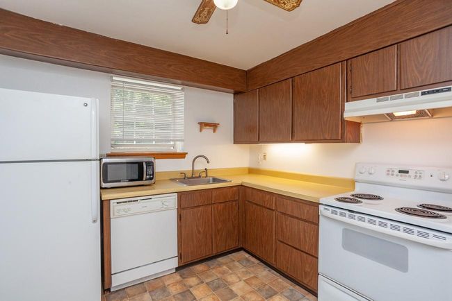 Kitchen featuring white appliances, under cabinet range hood, light countertops, a ceiling fan, and stone finish flooring | Image 9