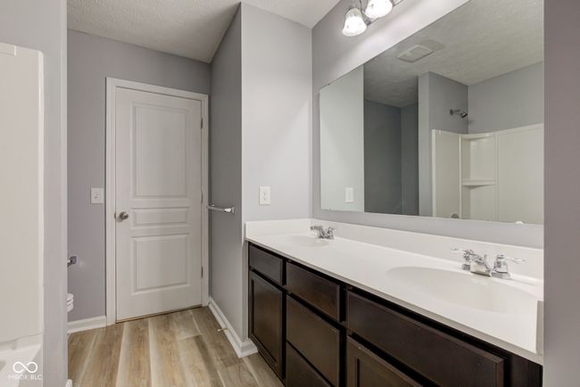 bathroom with wood finished floors, double vanity, a shower, and a textured ceiling | Image 41