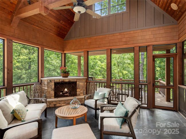 Screened porch is accessed off kitchen/dining area - features corner stacked stone gas log fireplace, ceiling fan with light, three skylights and built-in ceiling speakers. Door to partially covered deck with recessed lighting and outdoor speakers. Floor is slate tile. | Image 18