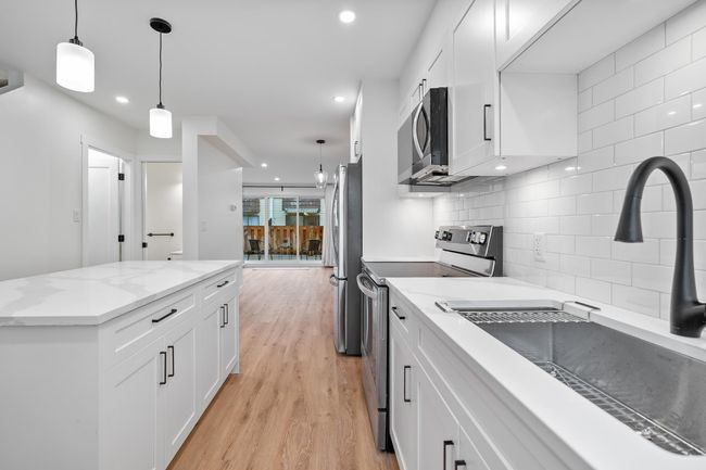 Kitchen featuring light wood-type flooring, decorative backsplash, appliances with stainless steel finishes, white cabinetry, and a sink | Image 4