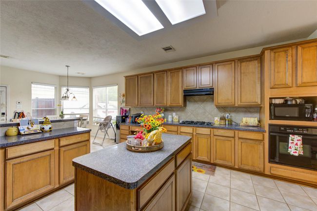 Bright and spacious kitchen with ample natural light, featuring wooden cabinets, granite countertops, and a central island. Equipped with modern appliances and a cozy dining nook with large windows. | Image 11