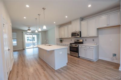 Kitchen with ceiling fan, stainless steel appliances, light hardwood / wood-style floors, and an island with sink | Image 1